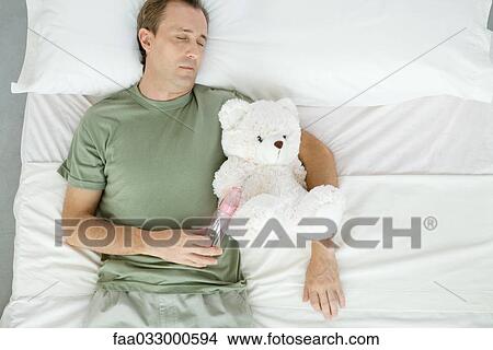 Picture - Father asleep in bed, holding baby bottle and teddy bear, overhead view. Fotosearch