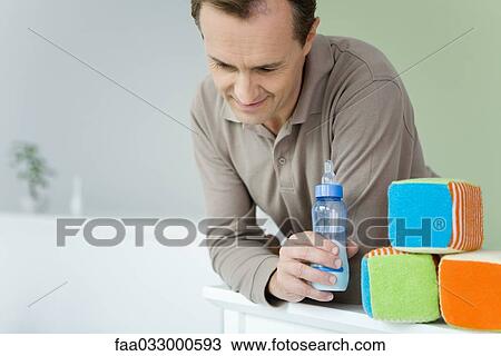 Father leaning against crib, holding baby bottle, looking down View Large Photo Image Stock Image - Father leaning against crib, holding baby bottle, looking down. Fotosearch