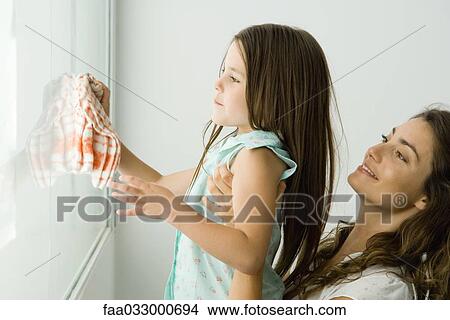 Picture - Girl cleaning window, mother holding her, both smiling. Fotosearch
