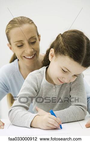 Stock Image - Girl drawing with crayon, mother looking over her shoulder and smiling. Fotosearch