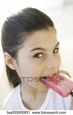 Stock Image - Girl eating frozen ice pop, looking at camera. Fotosearch
