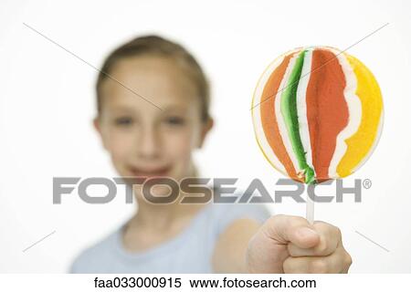 Stock Photography - Girl holding up and showing the camera a multicolored lollipop, focus on foreground. Fotosearch