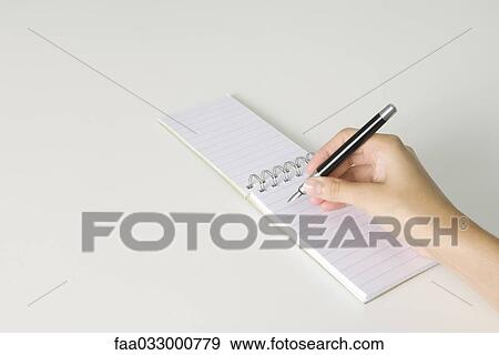 Stock Photo - Hand holding pen, poised to write in notepad flipped open, cropped view. Fotosearch