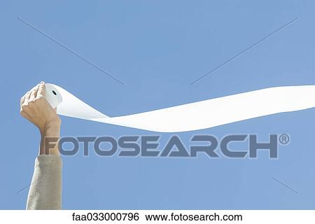 Stock Photograph - Hand holding toilet paper, unrolling in the breeze, cropped view. Fotosearch
