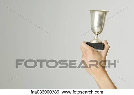 Stock Photo - Hand holding up trophy, cropped view. Fotosearch