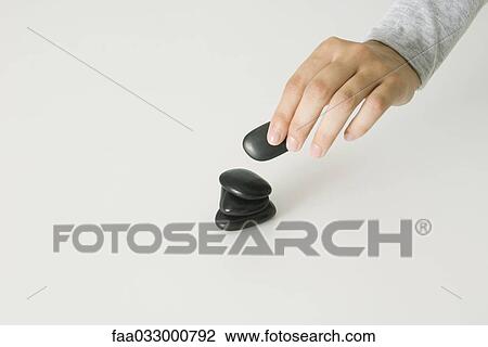 Stock Image - Hand stacking smooth black stones, cropped view. Fotosearch