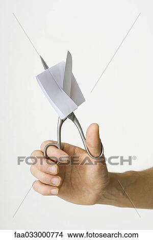 Picture - Hand using scissors to cut folded piece of paper, cropped view. Fotosearch