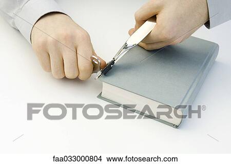 Picture - Hands using can opener on closed book, cropped view. Fotosearch