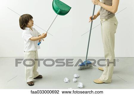 Stock Image - Little boy playing with dust pan while his mother is sweeping the floor, cropped view. Fotosearch
