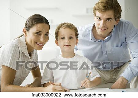 Stock Image - Little boy sitting with parents, drawing with pencil, all smiling at camera. Fotosearch