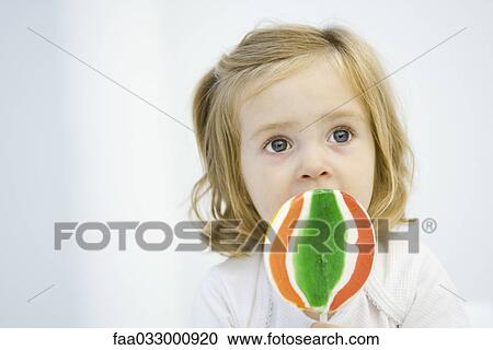 Stock Image - Little girl eating large lollipop, looking up. Fotosearch