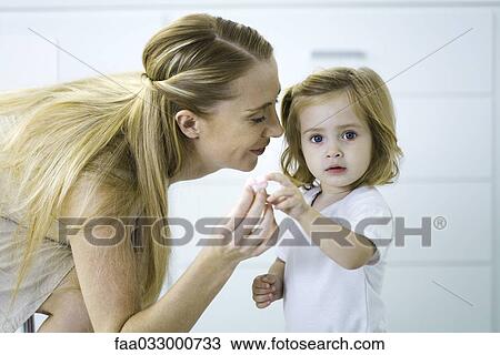 Stock Image - Little girl giving her mother a tiny heart, looking at camera. Fotosearch