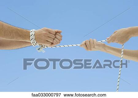 Stock Photo - Male hands bound by rope, female hands pulling rope, cropped view. Fotosearch