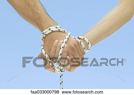 Man and woman holding hands, tied together with rope, cropped view View Large Photo Image Stock Photo - Man and woman holding hands, tied together with rope, cropped view. Fotosearch