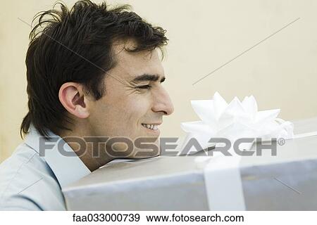 Stock Photo - Man carrying large present, eyes closed, side view. Fotosearch