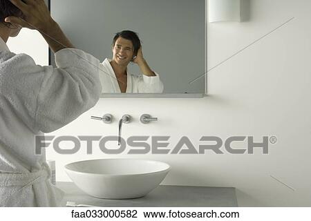 Stock Image - Man in bathrobe looking at self in bathroom mirror, hand in hair. Fotosearch