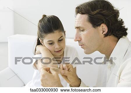 Man putting adhesive bandage on girl, both sitting on couch View Large Photo Image Stock Image - Man putting adhesive bandage on girl, both sitting on couch. Fotosearch
