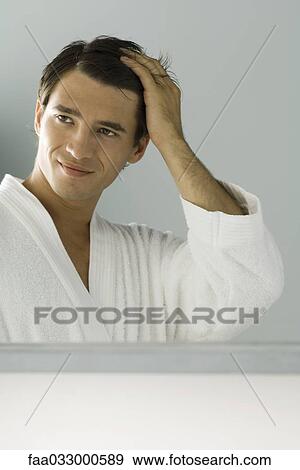 Stock Photo - Man smiling at self in mirror, hand in hair. Fotosearch