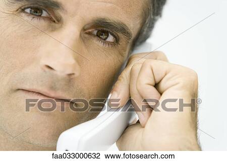 Stock Image - Man using phone, looking at camera, close-up. Fotosearch