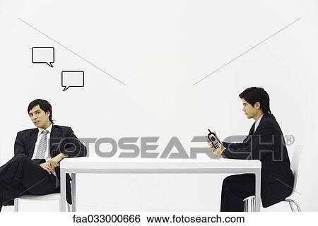 Stock Photograph - Man with word bubbles over head sitting across from second man with fake phone in hand. Fotosearch