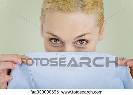 Stock Photography - Mother holding baby clothing in front of face, looking at camera. Fotosearch