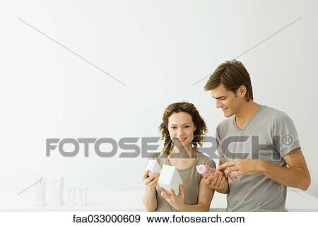 Stock Photo - New parents looking at milk cartons, man holding baby bottle, woman smiling at camera. Fotosearch