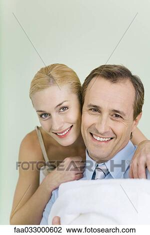 Stock Image - New parents smiling at camera, man holding wrapped up baby. Fotosearch