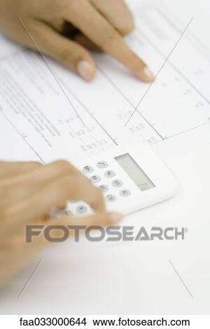 Picture - Person using calculator and pointing at document, cropped view of hands. Fotosearch