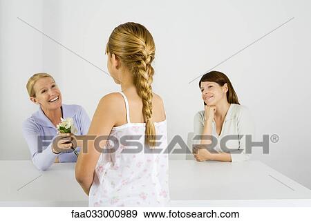 Preteen girl giving flower to her mother, another woman sitting nearby and smiling View Large Photo Image Stock Photo - Preteen girl giving flower to her mother, another woman sitting nearby and smiling. Fotosearch