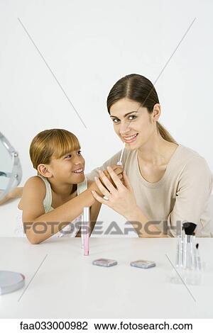Stock Image - Preteen girl putting make-up on her older sister, young woman smiling at camera. Fotosearch