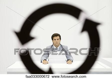 Stock Image - Professional sitting at desk with large stack of paper, circular arrow symbol in foreground. Fotosearch