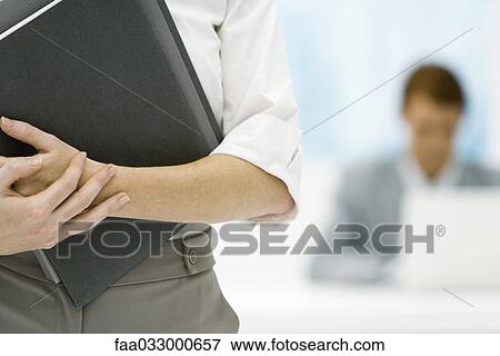 Professional woman holding binder, cropped view, male colleague in background View Large Photo Image Stock Photo - Professional woman holding binder, cropped view, male colleague in background. Fotosearch