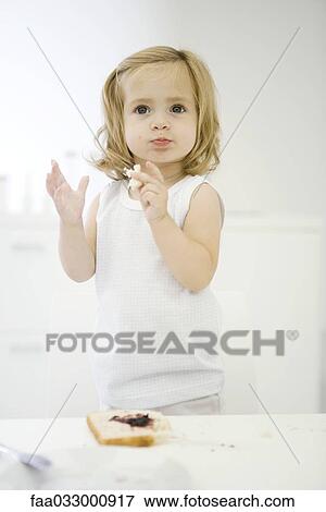 Stock Photo - Toddler girl standing on chair, eating bread with jam. Fotosearch