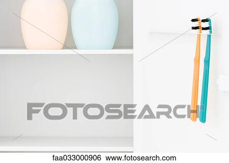 Stock Photograph - Toothbrushes hanging from toothbrush holder, bottles on shelf. Fotosearch