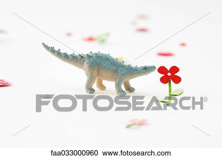 Stock Image - Toy dinosaur smelling artificial flower. Fotosearch