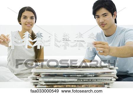 Stock Photo - Two young adults holding tree shapes cut out of newspaper, smiling at camera. Fotosearch
