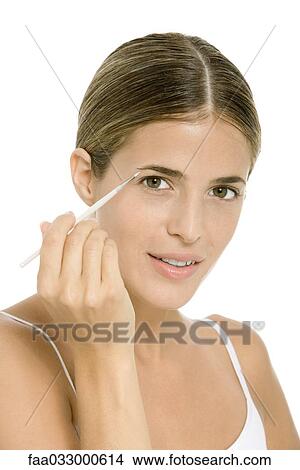 Picture - Woman applying eye make-up with brush, looking at camera. Fotosearch