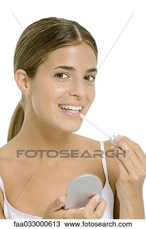 Stock Image - Woman applying lip gloss, smiling at camera. Fotosearch