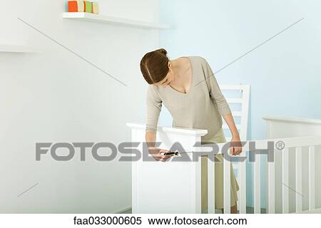 Stock Photography - Woman assembling crib in nursery. Fotosearch