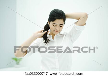 Stock Photo - Woman fixing hair, holding hairpin in mouth, looking down. Fotosearch