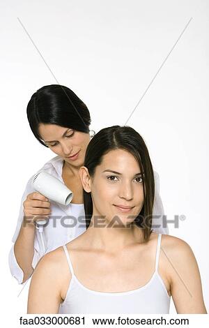 Stock Image - Woman having hair dried by stylist, smiling at camera. Fotosearch