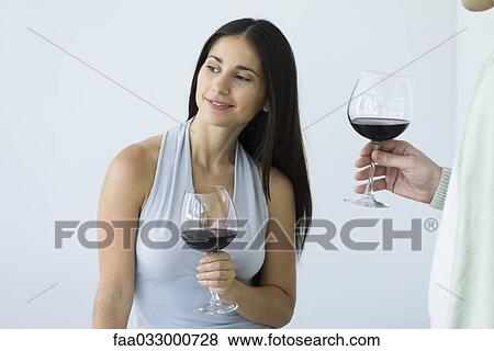 Stock Photo - Woman holding glass of wine and looking away, man standing nearby, cropped view. Fotosearch
