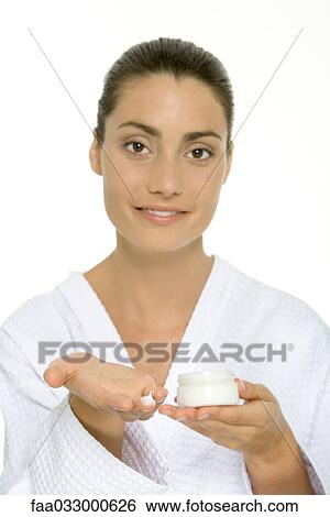 Stock Photograph - Woman in bathrobe holding moisturizer on hand, smiling at camera. Fotosearch