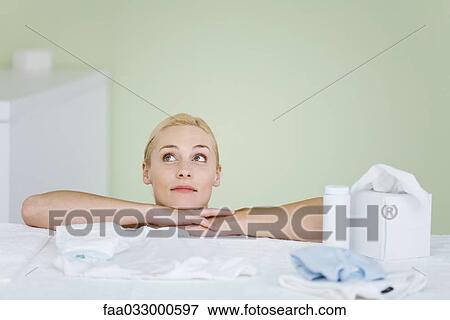Stock Photo - Woman in nursery, resting head on arms, looking up, smiling. Fotosearch