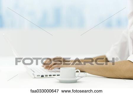 Woman using laptop computer, coffee cup nearby, cropped view View Large Photo Image Stock Photo - Woman using laptop computer, coffee cup nearby, cropped view. Fotosearch