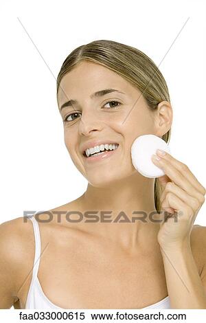 Stock Photography - Woman wiping face with cotton cosmetic pad, smiling at camera. Fotosearch