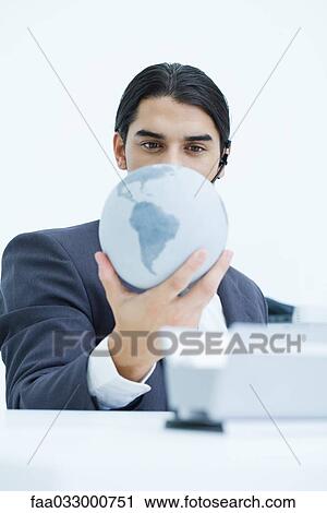 Stock Image - Young businessman holding globe and looking down at it. Fotosearch