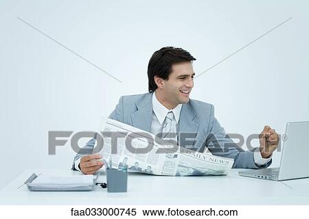 Young businessman looking at laptop and smiling, holding newspaper and clenching fist View Large Photo Image Stock Photography - Young businessman looking at laptop and smiling, holding newspaper and clenching fist. Fotosearch