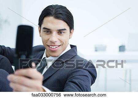 Young businessman using cell phone to take picture of himself, smiling View Large Photo Image Stock Photograph - Young businessman using cell phone to take picture of himself, smiling. Fotosearch