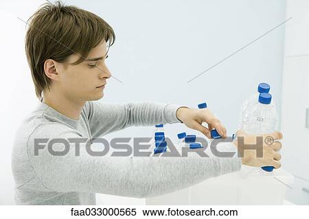 Stock Photography - Young man placing plastic bottle in recycling bin, side view. Fotosearch